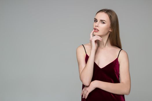 Young model long-haired blond girl in dard red dress poses showing emotions