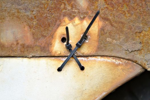 Detailed photo of two cable ties holding a rear bumper of old very rusty car.