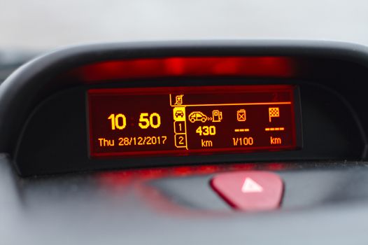 On board computer showing date and time, fuel consumption info and trip length in kilometers. Also hazard warning lights button visible on foreground.