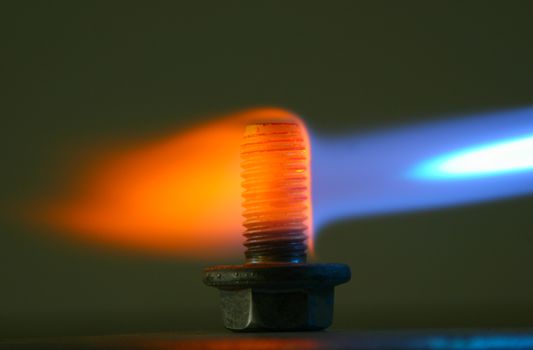 Hardening an iron bolt in home conditions with the gas torch. Close image of blue flame turning yellow as temperature drops.