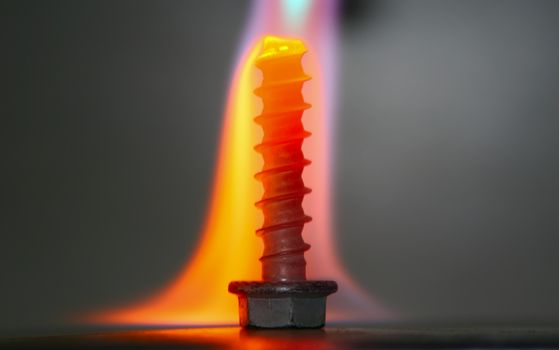 A threaded bolt in the gas flame. Flame changes it's color as it cools down after touching cold metal.