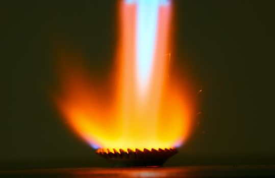 Flame reflects from toothed washer as it is heated with the flame of a gas torch. Technical closeup photo with dark background.