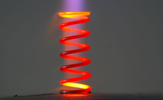 Technical closeup of a steele coil spring heated up to extreme temperatures so metal has changed it's color. Part of the gas flame still visible on the picture with smooth dark background.