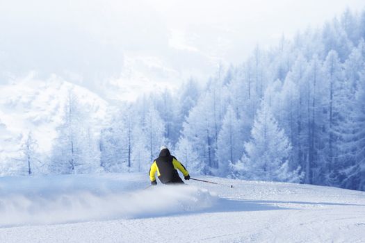 Alpine skier on piste running downhill in beautiful Alpine landscape. Blue sky on background. Free copy space for text