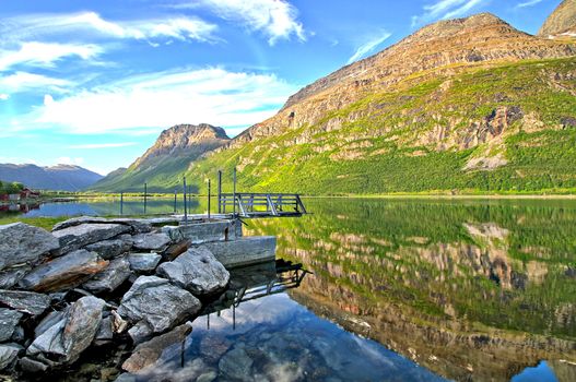 One boat dock by the sea in the morning. Colorful mountains reflecting from water surface.