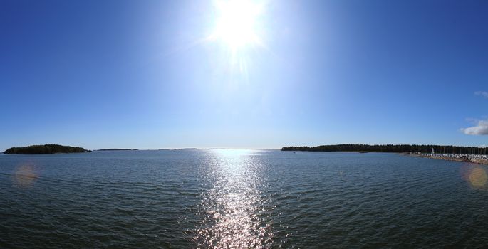 Sun shining high above blue water surface causing sun flare at both edges of the photo.