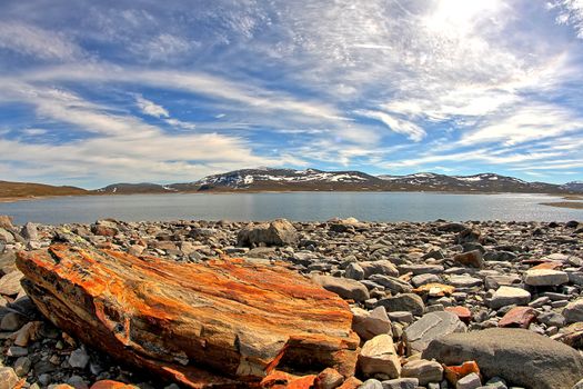 Beautiful landscape with mountains and a lake. A heavy rusty rock on the foreground