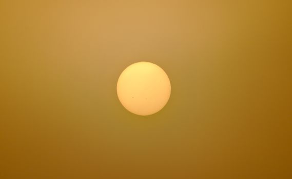 Dark yellow sun shining through misty air. Air pollution has reduced the brightness of the sun so it can be watched even without sunglasses.