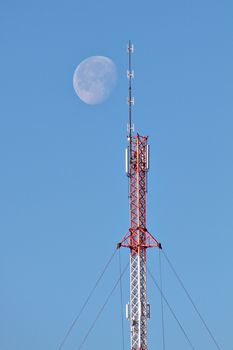 Large moon shining next to top of a telecommunication tower at daytime. Communication to the moon and space. Maybe receiving extraterrestrial signals from other civilizations.