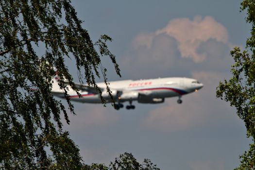 A white airplane with red stripes preparing to land. Photo taken through the trees, airplane blurred on background.