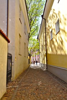 Narrow street between historic buildings in Old Town of Tallinn. Two people walking down the street.