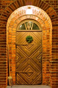 Lighted entrance with old decorated wooden door. Round top and small window above the door. Surrounded with stone walls.