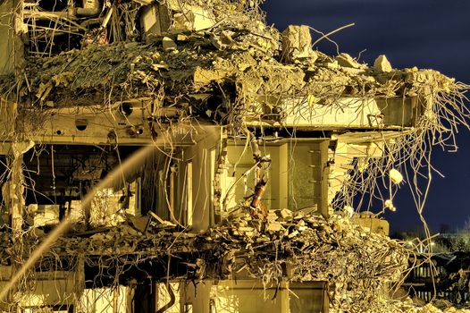 Ruins of an office building with rooms and floors visible through the wall. Cables and pipes hanging, water still flowing from pipes. Dramatic night scene.