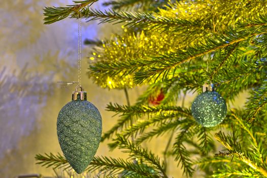 Closeup of sparkling green / blue cone shaped decoration hanging on a Christmas tree. Another ornament and golden decorations on background