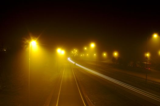 Fog and low visibility on motorway at night. Bad weather conditions for driving. Some cars passing, leaving light trails.