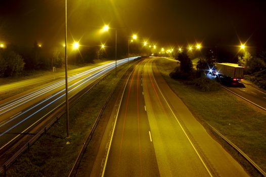Foggy night on the motorway with some cars passing leaving light trails.