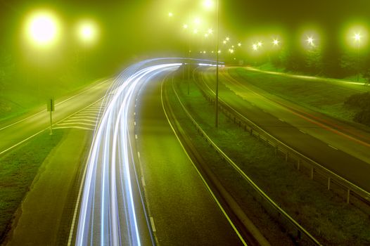 Bright light trails of headlights of passing cars at misty night on the highway. Long exposure photo of traffic on motorway in the dark.