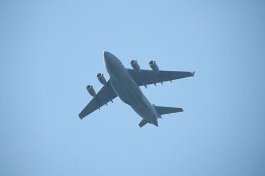 Four engine military cargo plane flying in the air. Dark grey plane silhouette with four jet engines, blue sky on the background.