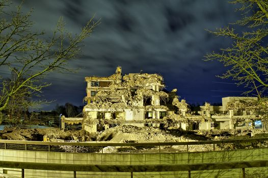 An apocalyptic view of ruins of an office building in the dark with no roof and walls. Interior visible through collapsed walls.