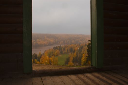 Look out the door it's autumn. Yellow forest landscape seen from dark room on the high ground.