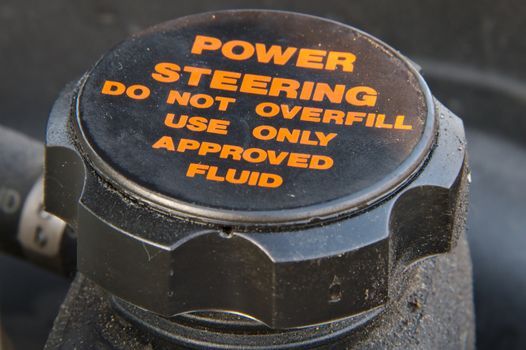 Closeup of a cap of a power steering oil tank. Do not overfill and use approved fluid only warning text.
