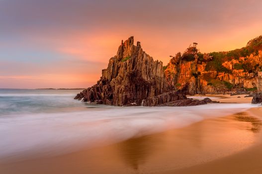 Beautiful sunrise light at Bingie Beach with soft motion flows around the pyramid rock sea stack