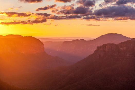 Scenic sunrise with stunning golden light streaming into the valley - the imposing Mt Hay rising up  in the distance.  Blue Mountains Australia
