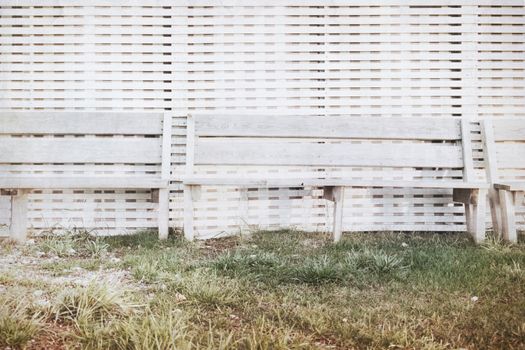 Bench stand at a wall from white colored boards at sunset by the sea