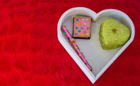 Valentines day decorations background, a white heart shaped box with a pen, note book and heart shaped box laying on a red pillow