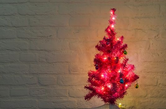 lighted and decorated christmas tree isolated on a white brick wall background