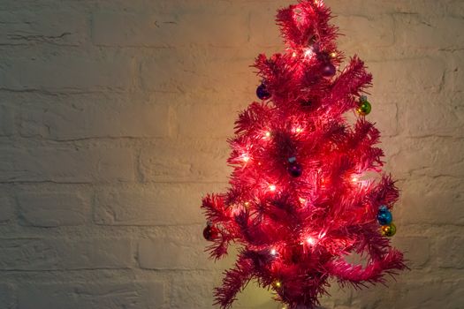decorated christmas tree with lighted lights isolated on a white brick wall background