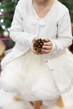 Christmas time. A little girl holds a golden cone in front of the Christmas tree.