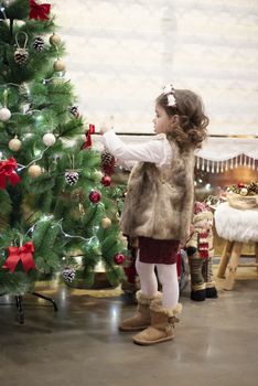 Little child girl decorating Christmas tree with balls at home, indoors. Close up. Christmas concept.