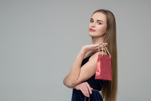 Young model long-haired blond girl in dark blue dress holds red paper gift present package