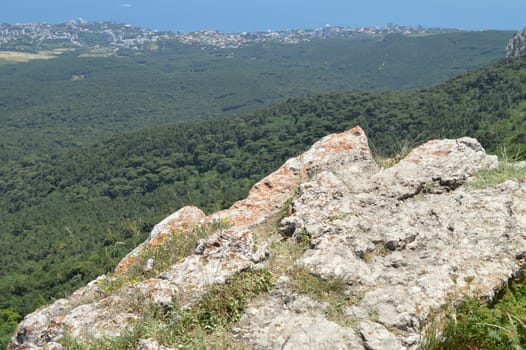 THE VIEW FROM THE ROCKY TOP OF THE MOUNTAIN TO THE PINE FOREST AND THE SEASIDE TOWN.