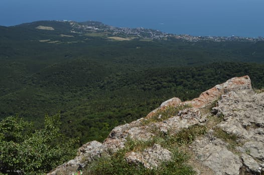 THE VIEW FROM THE ROCKY TOP OF THE MOUNTAIN TO THE PINE FOREST AND THE SEASIDE TOWN.