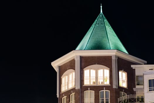 beautiful city tower building with lighted apartment windows and a pointy rooftop, modern dutch architecture at night