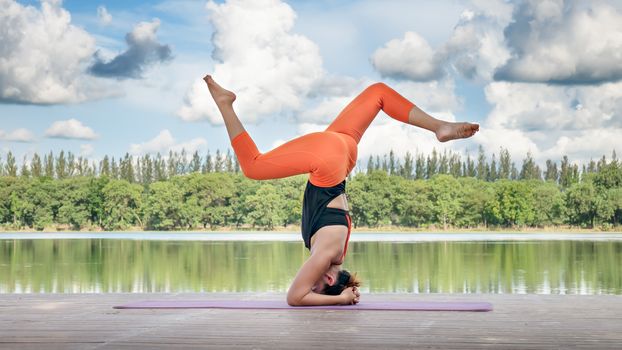 Asian woman practicing yoga pose , exercise outdoors with view of beautiful lake - relax in nature