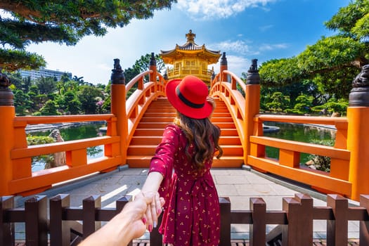 Women tourists holding man's hand and leading him to Golden Pavilion in Nan Lian Garden near Chi Lin Nunnery temple, Hong Kong.