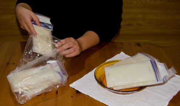 mother packing frozen breast milk in bag for further storage in freezer, woden table