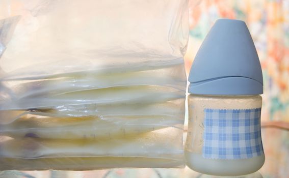 frozen breast milk in storage bags and baby bottle with fresh expresed milk