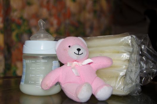 baby bottle with fresh expresed breast milk, frozen breastmilk in storage bags and soft toy pink teddy bear, breastfeeding concept