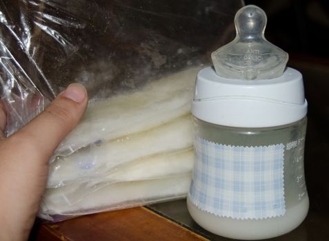 woman hand holding frozen breast milk in storage bags and baby bottle with fresh expresed breastmilk, breastfeeding concept