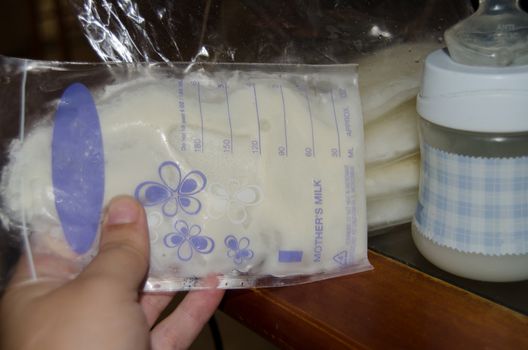 woman hand holding frozen breast milk in storage bags and baby bottle with fresh expresed breastmilk, breastfeeding concept