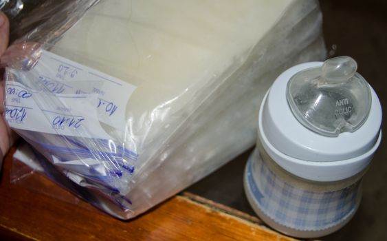 frozen breastmilk in storage bags and baby bottle with fresh expresed breast milk on wooden table, breastfeeding concept