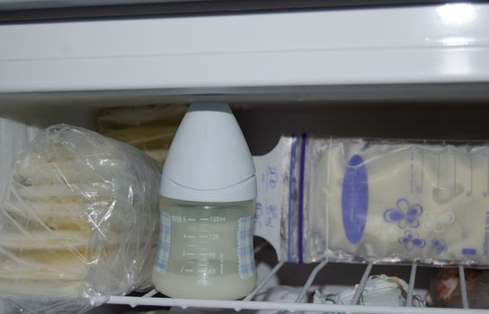 lot of frozzen breast milk in storage bags stored in the freezer and baby bottle with fresh expresed breastmilk, smille, breastfeeding concept