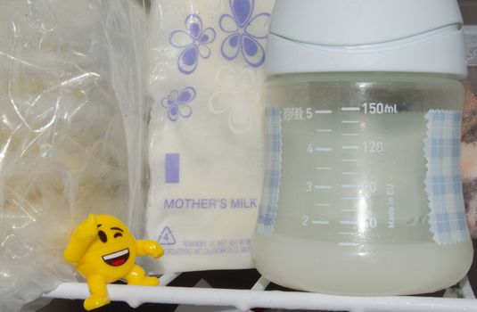 lot of frozzen breast milk in storage bags stored in the freezer and baby bottle with fresh expresed breastmilk, smille, breastfeeding concept