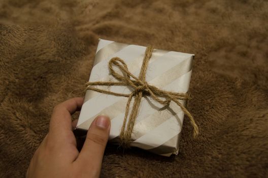 woman hand holding a gift box against brown background