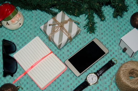 preparing for christmas at work concept flat lay with phone, notebook, gift, christmas ornaments, watch