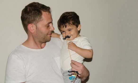 Father and son playng with moustache funny face expressions, family time